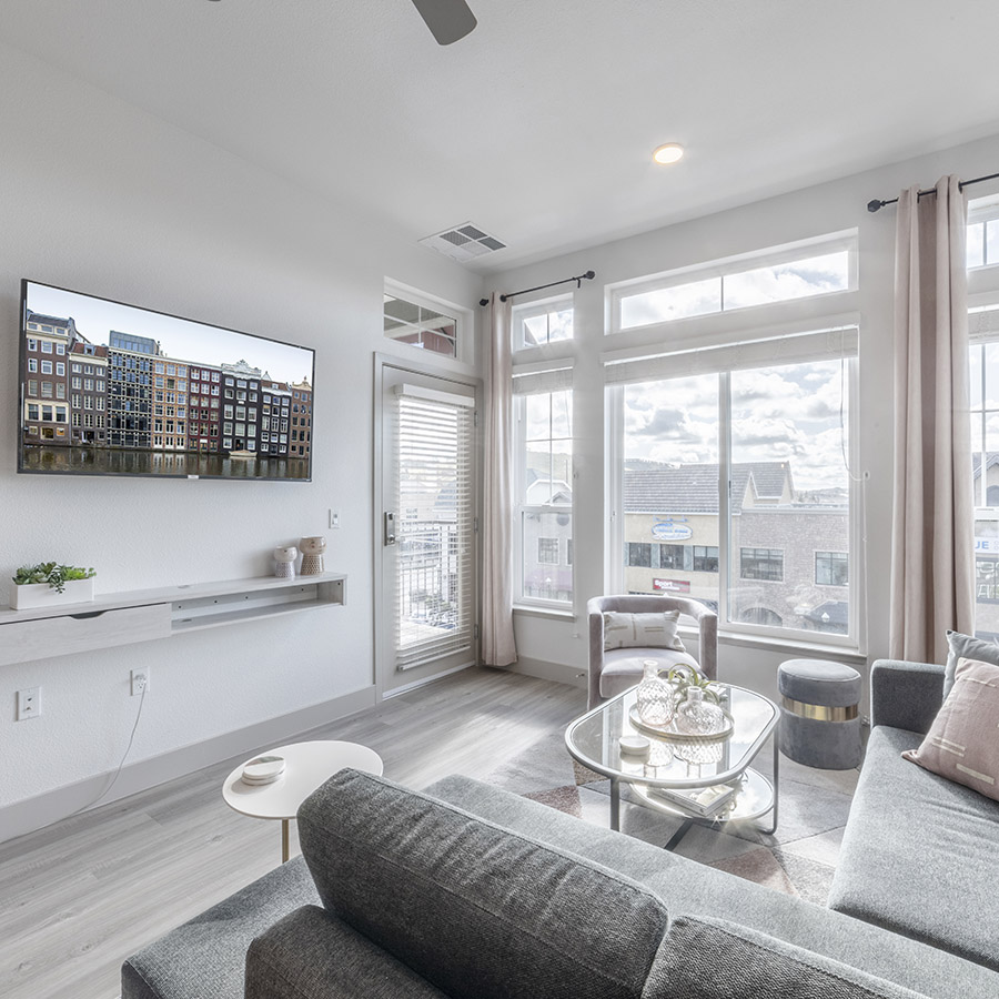 Living room with wood floor, plush couch, wall mounted TV, and door to balcony.